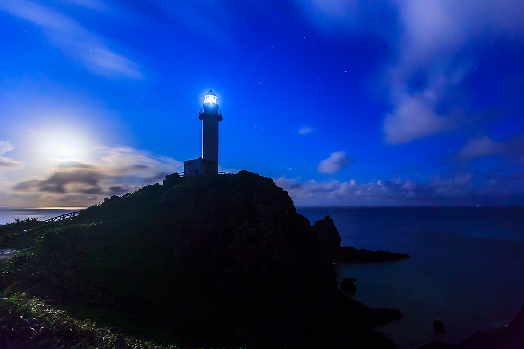 Lighthouse on hill under dramatic moonlit sky