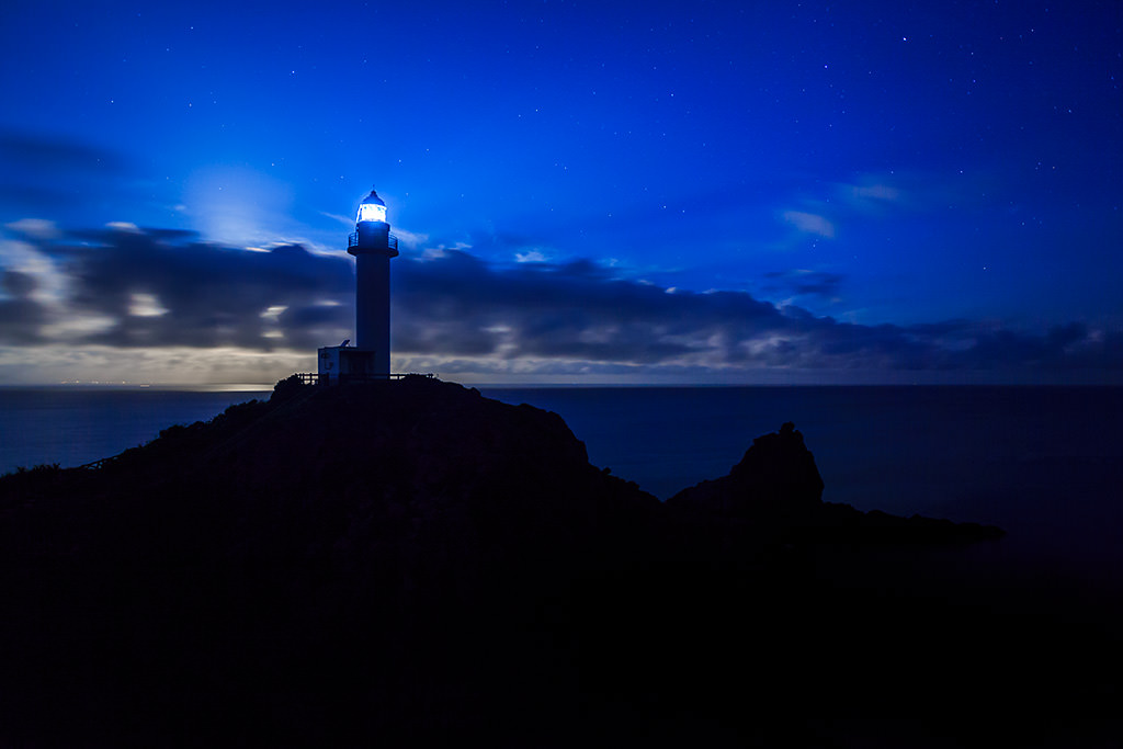 Lighthouse on hill under night sky with no moon