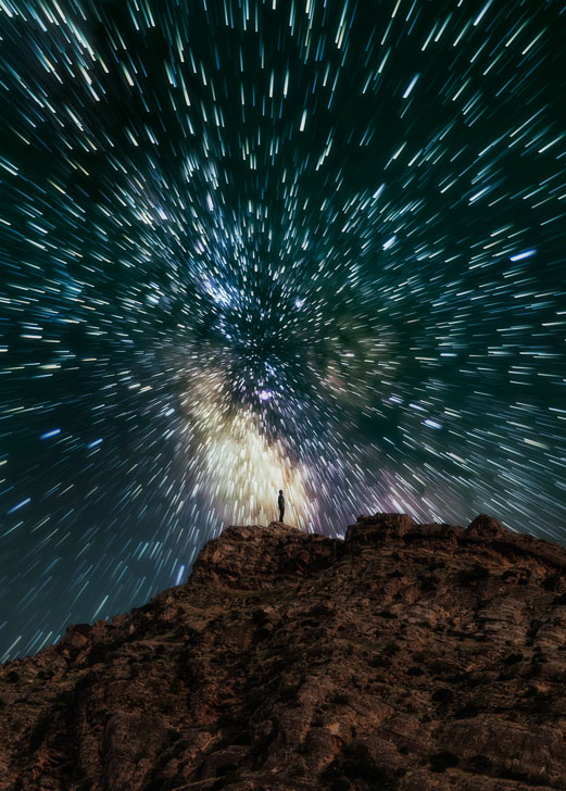 photographer standing on top of cliff against a circular star trail