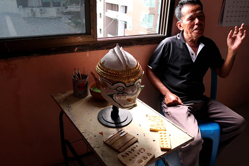 Prateep Rodpai sitting by a window in his Bangkok studio, with a partially completed mask and all his tools.