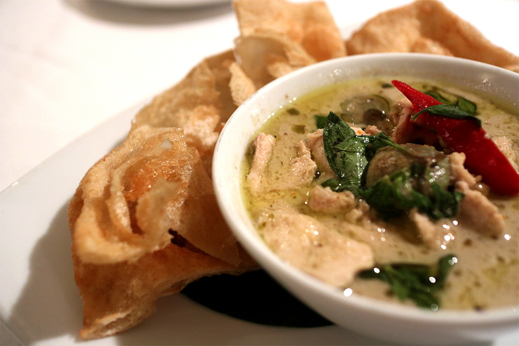 Green chicken curry accompanied by a serving of fried Indian bread.