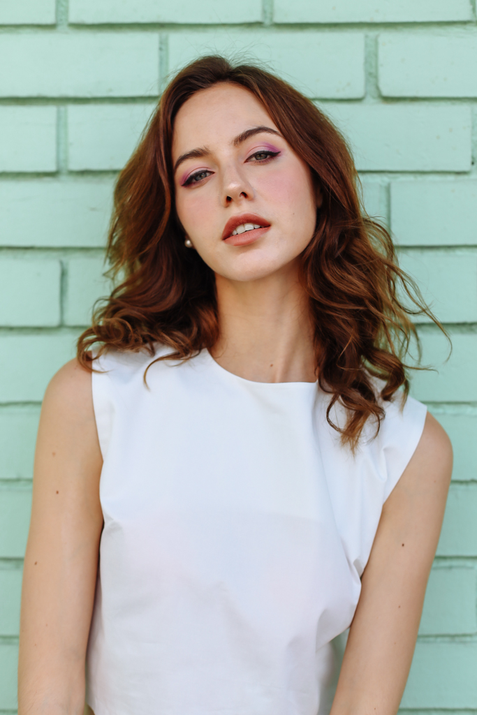 female in white top in front of green wall portrait 