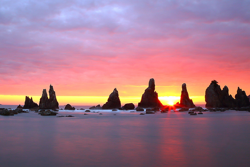Slow shutter shot of rocks in sea against sunrise