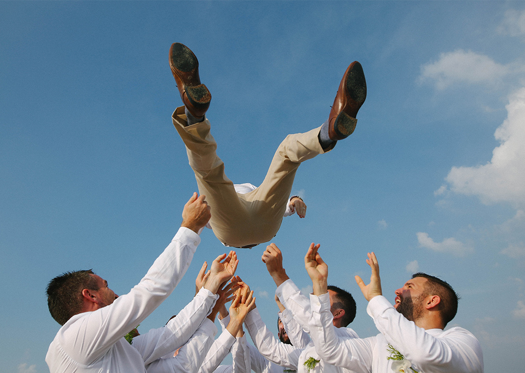 Groom being thrown in the air by groomsmen