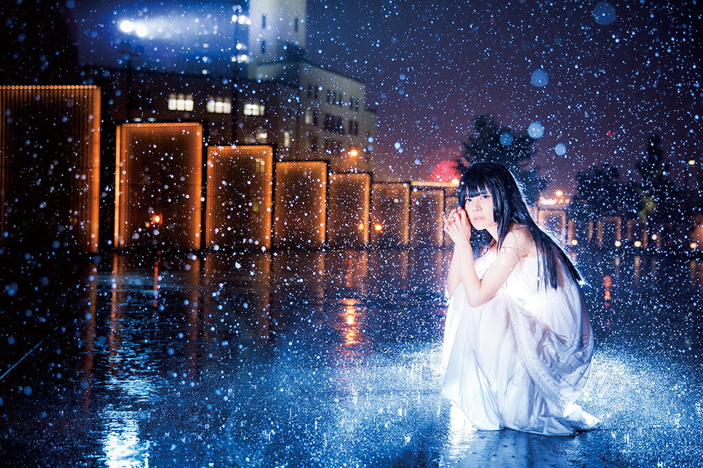 Model in white crouching in front of night scenery in the rain