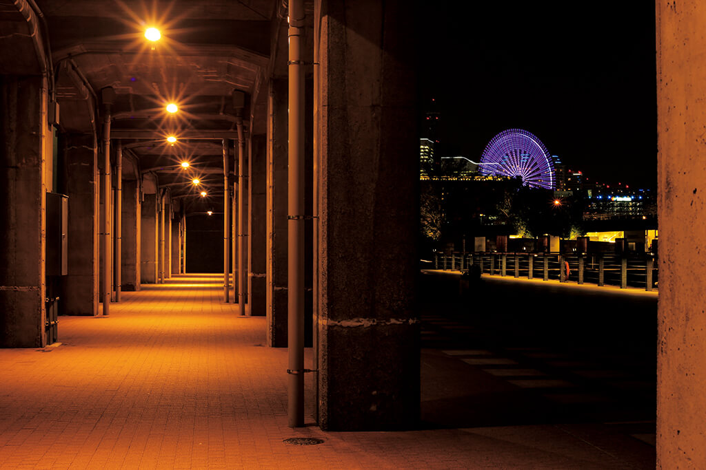 Night shot of warmly-lit corridor under a bridge with Ferris wheel in the background