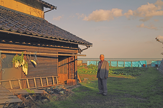 Man standing next to hut. Shadows lifted, mostly mid-tones