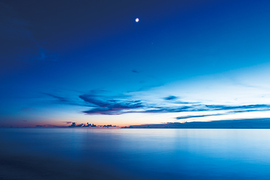 Blue seascape with moon and a bit of red sunset
