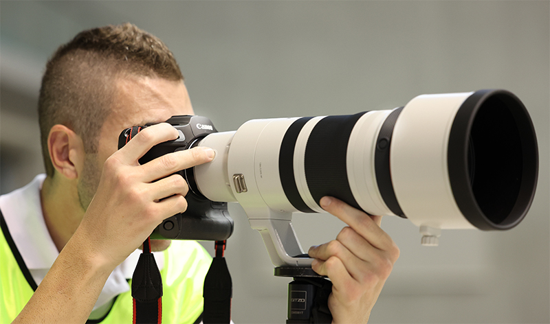 Photographer with finger on the lens function button, holding the grip.